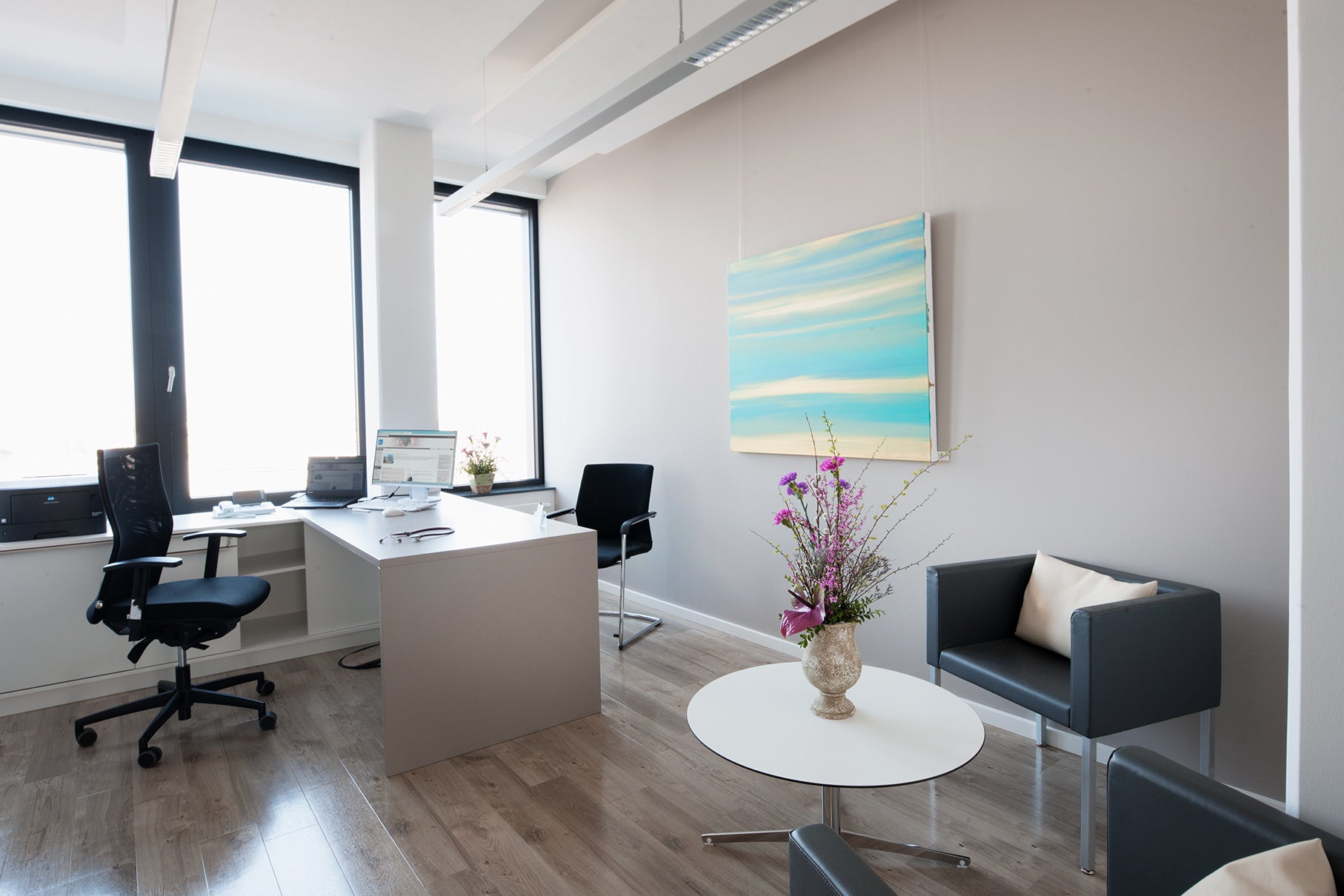 Ein Behandlungsraum der ias PREVENT in Chemnitz. Es ist ein Schreibtisch zu sehen an dem von beiden Seite jeweils ein Stuhl steht. Im Vordergrund ein Tisch mit einer Vase und Pflanzen im Hintergrund an der Wand ein Bild.