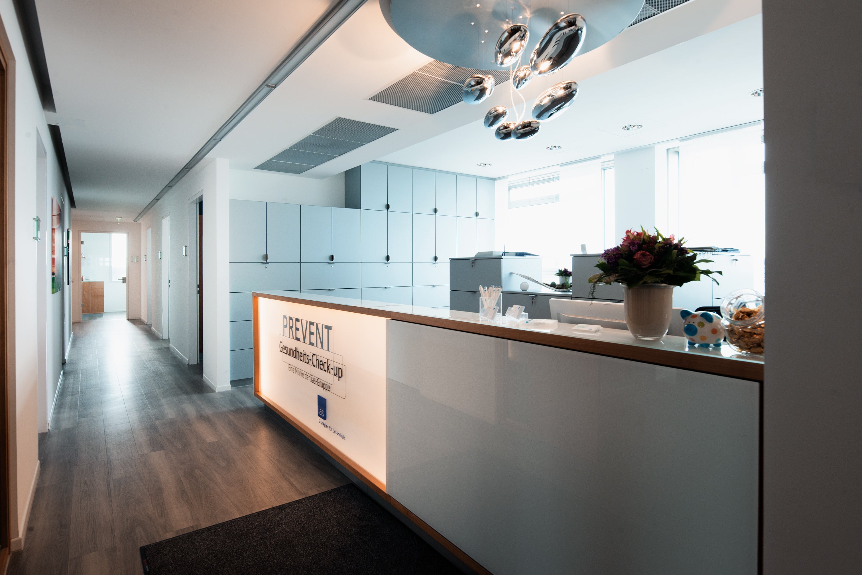 Der Eingangs Bereich der ias PREVENT in Hamburg. Es ist eine Empfangstheke zu sehen mit dem ias-Logo. Daneben ein langer Gang mit einigen Türen.
