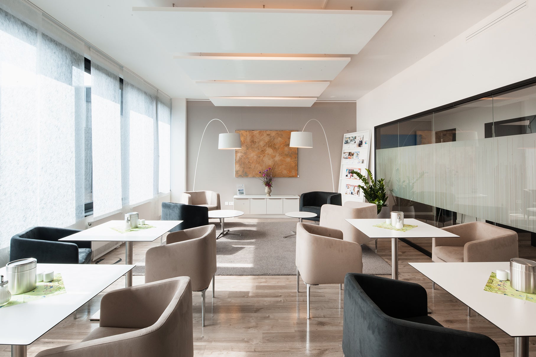 Der Wartebereich der ias PREVENT in München. Es sind mehrere Tische zu sehen an denen Stühle stehen. Es liegt ein Teppich auf dem Boden und am hinteren Ende des Raumes sind Sessel platziert.